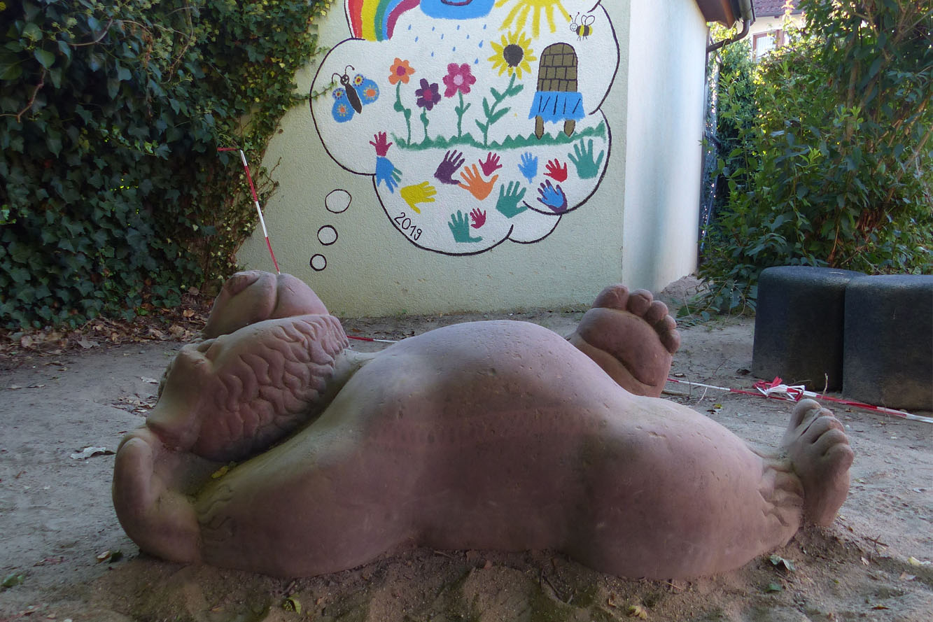 Steinskulptur liegender Bär im Sandkasten
