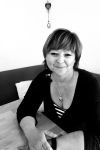 Portrait von Frau Schinhofen - sie sitzt am Tisch und lächelt in die Kamera